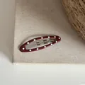 Vue détaillée d'une pince à cheveux ovale rouge à pois sur une surface en tissu texturé. - Clip BB Ovale à Pois / Rouge Brique