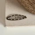 Gros plan d'une pince à cheveux ovale marron à pois blancs sur fond de tissu - Clip BB Ovale à Pois / Café