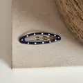 Gros plan d'une pince à cheveux ovale bleue à pois blancs sur fond en lin beige - Clip BB Ovale à Pois / Bleu