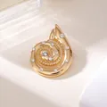 Nahaufnahme einer goldfarbenen Muschel-Brosche mit funkelnden Strasssteinen auf hellem Grund - Gold Muschel Spirale Strass Stil (A20-110)