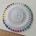 Vue de dessus de quarante épingles à tête perle colorées disposées sur un disque à roue blanc - Épingles à Perles Roue (TZA006) / Pack de 40 / Coloré