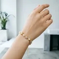 Elegante bracciale in oro con perle bianche e ciondoli floreali scintillanti sul polso - Bracciale