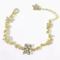 Dettaglio ravvicinato di un bracciale dorato con fiori e foglie e strass di cristallo - Bianco