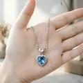 Dettaglio ravvicinato di una collana con ciondolo a cuore in cristallo blu tenuta in mano - Collana / Blu