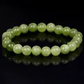 Macro view of a natural green jade bead bracelet on a reflective black background - Olivine Jade