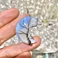 Close-up view of a handcrafted wire-wrapped moon opal pendant with a tree of life design. - Opal