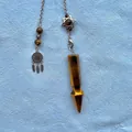 Detailed view of a tiger eye stone crystal pendulum with decorative silver-tone chain. - Tiger Eye Arrowhead Pendulum