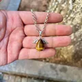 Macro view of natural tiger's eye teardrop pendant with silver angel wings in palm - Pendant Only (No Chain) / Tiger's Eye