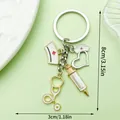 Medical themed keychain with syringe and stethoscope charms, dimensions 8cm x 3cm. - Double Nurse Hat Syringe Stethoscope Keychain (LS588)