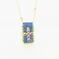 Dettaglio squisito della collana a croce bohémien con zirconi viola su un ciondolo in denim blu - Viola (C)