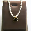 Detail shot of pearl necklace featuring a black suitcase pendant with Love Travels - Black