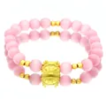 Close-up of pink cat's eye stone bracelet with golden dragon charm on reflective surface - Cat-eye Stone Bracelet / Pink