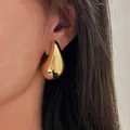 Primer plano detallado de un elegante pendiente de botón de gota dorado en la oreja. - Pendientes de Botón de Gota de Agua Dorados (A5221_1)
