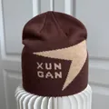 Detailansicht einer braunen Strickmütze mit beigem Xun Gan Design und Schriftzug - M / Kaffeebraun