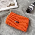 Nahaufnahme des orangefarbenen Strickstirnbands mit Rippstruktur und Buchstaben-Patch - Orange