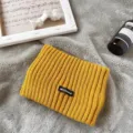 Makro-Detailansicht des gelben gerippten Strickstirnbands mit schwarzem Markenaufnäher - Kurkuma