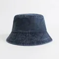 Vista dettagliata della trama in denim lavato e dell'occhiello in ottone su un cappello a secchiello - Blu navy