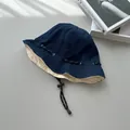 Detailed view of retro denim bucket hat with adjustable drawstring and cream lining. - Reversible / Navy and Beige