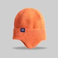 Detail view of an orange knitted winter beanie with earflaps and snowflake tag. - Elastic Circumference (56-59cm) / Orange