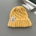 Dettaglio di un berretto in maglia a treccia giallo con un'etichetta in tessuto bianco - Giallo