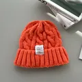 Dettaglio di un berretto invernale arancione in maglia a trecce con toppa in tessuto bianco - Arancione