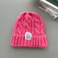 Berretto in maglia a trecce rosa acceso con etichetta tessuta su sfondo minimalista. - Rosa intenso