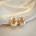 Close-up of baroque pearl earrings with delicate golden lily of the valley floral detail. - May - Lily