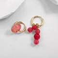 Detail of asymmetrical gold hoop earrings with red textured stone beads on a white surface. - Pink Textured Round Bead Style (21855_2)