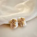 Close-up of baroque pearl earrings with golden flower detail on white silk background - January - Carnation