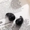 Boucles d'oreilles clous noires brillantes en forme de goutte sur fond de livre. - Noir