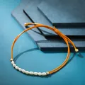 Dettaglio macro di un braccialetto intrecciato arancione con perle d'acqua dolce bianche. - Perla Artificiale Arancione
