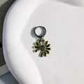 Vista macro di un pendente vintage a margherita dorata su un cerchio in metallo argento lucido - Orecchini a cerchio con fiori / Oro