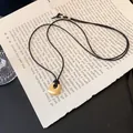 Nahaufnahme einer quadratischen Goldkette auf einer alten Buchseite im schicken Vintage-Stil - Quadratischer Plaketten-Anhänger / Gold