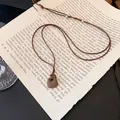 Detailaufnahme einer minimalistischen quadratischen Steinkette auf alten Buchseiten - Quadratischer Plaketten-Anhänger / Braun