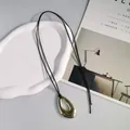 Nahaufnahme eines goldenen ovalen Anhängers an einer schwarzen Lederkette. - Hohlwassertropfen-Stil / Gold