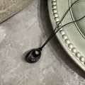 Nahaufnahme einer schwarzen Tropfen-Halskette mit glänzendem Finish auf grauem Stein - Bohnenanhänger (Schwarze Wachsschnur) / Schwarz Stil