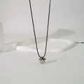 Nahaufnahme eines minimalistischen silbernen Blumenanhängers an einem schwarzen Choker - Wachsschnur Blumen-Stil / 85cm Schwarze Schnur