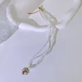 Nahaufnahme einer dreireihigen Perlenkette mit lila emailliertem Blumenanhänger - Vierblättrige Blume