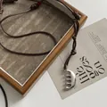 Macro view of a creative stainless steel comb pendant necklace with a brown cord. - Knotted Brown Wax Cord / Silver