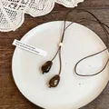 Detailed view of amber teardrop pendants on an adjustable dark brown cord necklace. - Amber