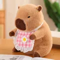 Lindo peluche de capibara marrón con babero de flores a cuadros rosa en mesa de madera - Bebé Carpincho Rosa