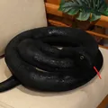 Realistic black snake plush toy prank prop with detailed scale texture on a chair - Black