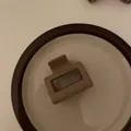 Vista de detalle de una pinza geométrica beige mate sobre una bandeja minimalista - Pinza Cuadrada Pequeña / Café