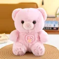 Front view of pink plush teddy bear with rotating heart-shaped badge detail - 22cm / Pink