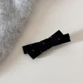 Vue détaillée d'une barrette à nœud noir à pois sur un fond en tissu gris doux - Barrette / Noir