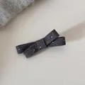 Gros plan d'une pince à cheveux en forme de nœud en laine grise à pois sur fond neutre - Barrette / Gris