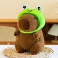 Detail shot of a cute capybara plush toy wearing a bright green frog hat on a mat. - 25cm / Frog Hat Capybara