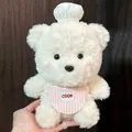 Vue détaillée d'un ours en peluche chef de 20 cm avec chapeau blanc et tablier rose - Ours Chef Blanc Cassé (1) / 22cm