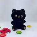 Close-up of a cute fluffy black cat plush toy with large golden eyes on a desk - 22cm / Black