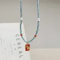 Makroansicht einer blauen handgefertigten Perlenkette mit rotem Emaille-Anhänger - Goldenes Pferd Anhänger Stil / 45+5cm / Blau